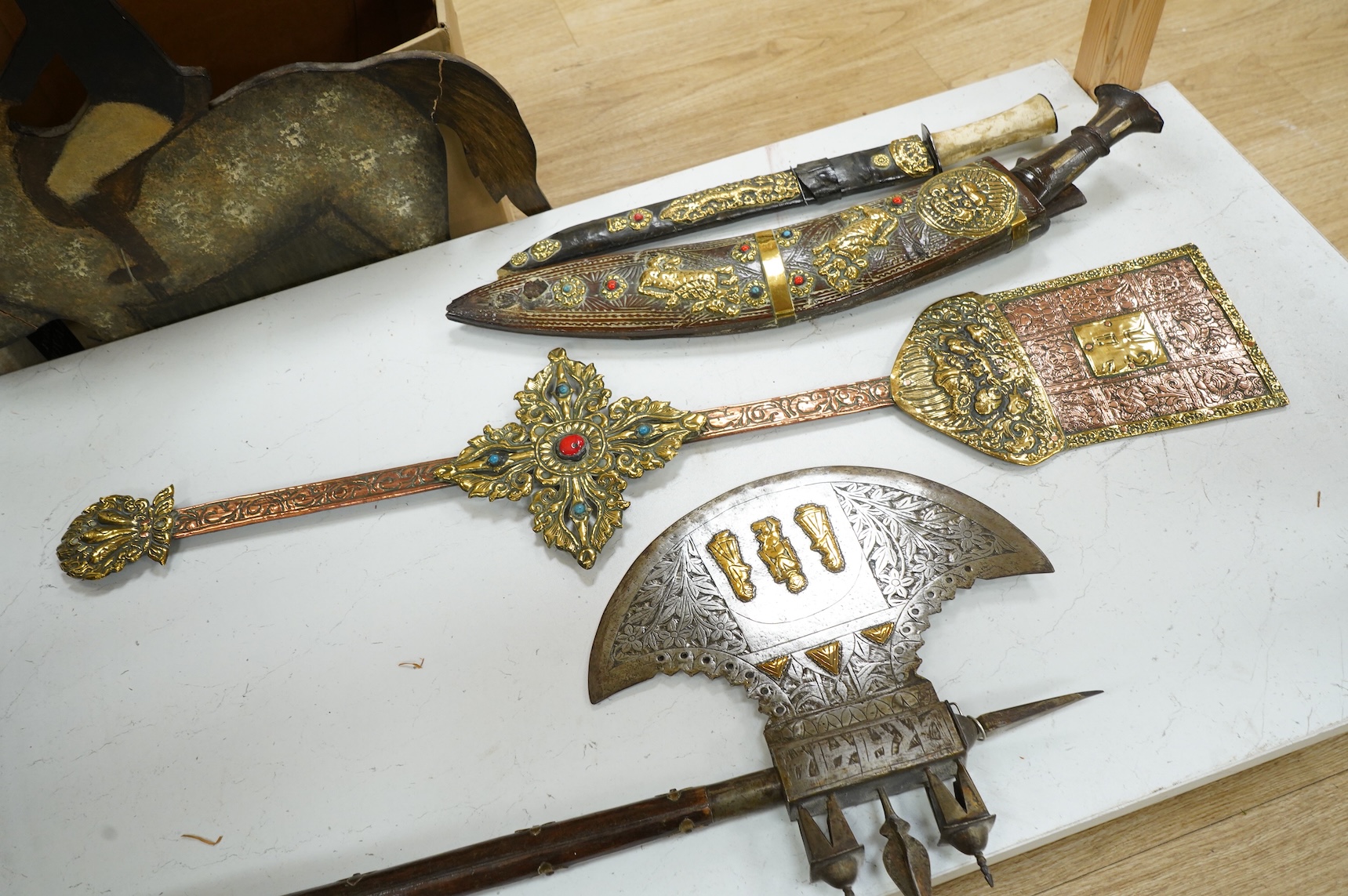 A decorative Indian axe, the large head inlaid with brass Hindu figures, together with a brass mounted North Indian kukri, another similar knife with bone handle, and a large shovel-shaped copper and brass item possibly